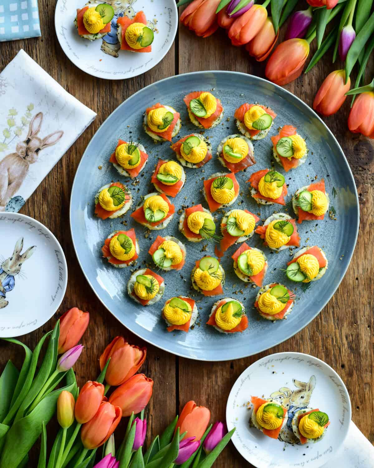 Colorful Easter deviled eggs on platter surrounded with Easter decoration.