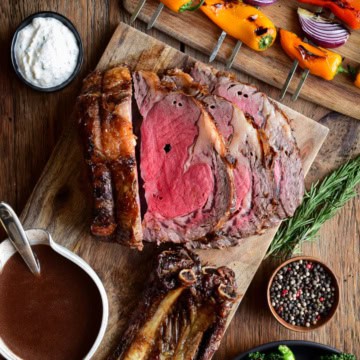 A sliced rotisserie prime rib roast served with gravy, horseradish sauce, and grilled veggies.
