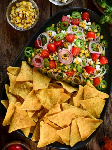 A platter of Guacamole with Grilled Corn and chips.