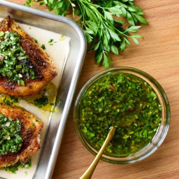 A bowl of a quick chimichurri recipe sauce with two chicken breasts and parsley.