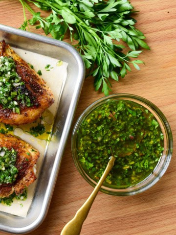 A bowl of a quick chimichurri recipe sauce with two chicken breasts and parsley.