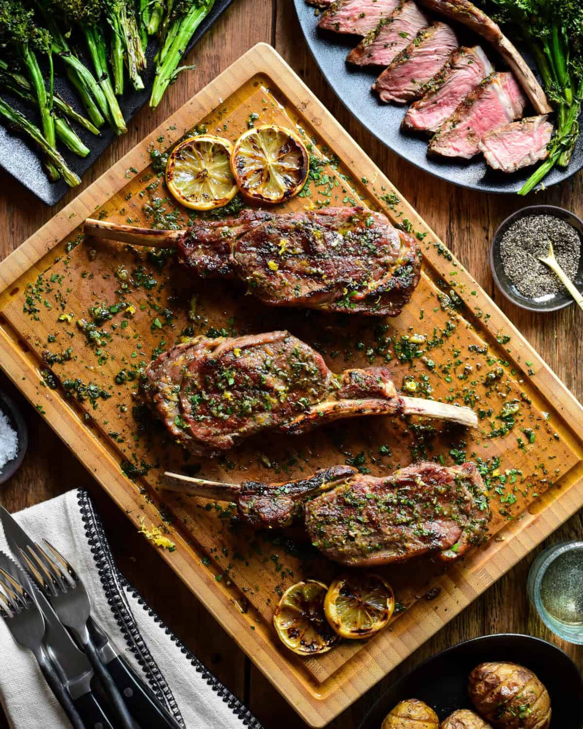 Three Tuscan style veal chops on a cutting board with sauce. A sliced chop is served with a potato and broccolini.