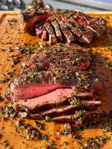 A medium-rare T-bone is sliced and on a board with a peppercorn sauce.