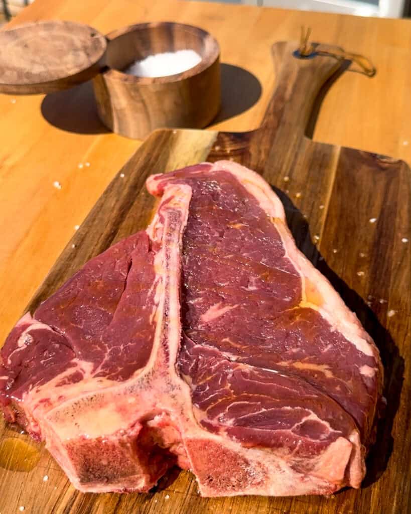 A T-bone steak about to get seasoned with salt.