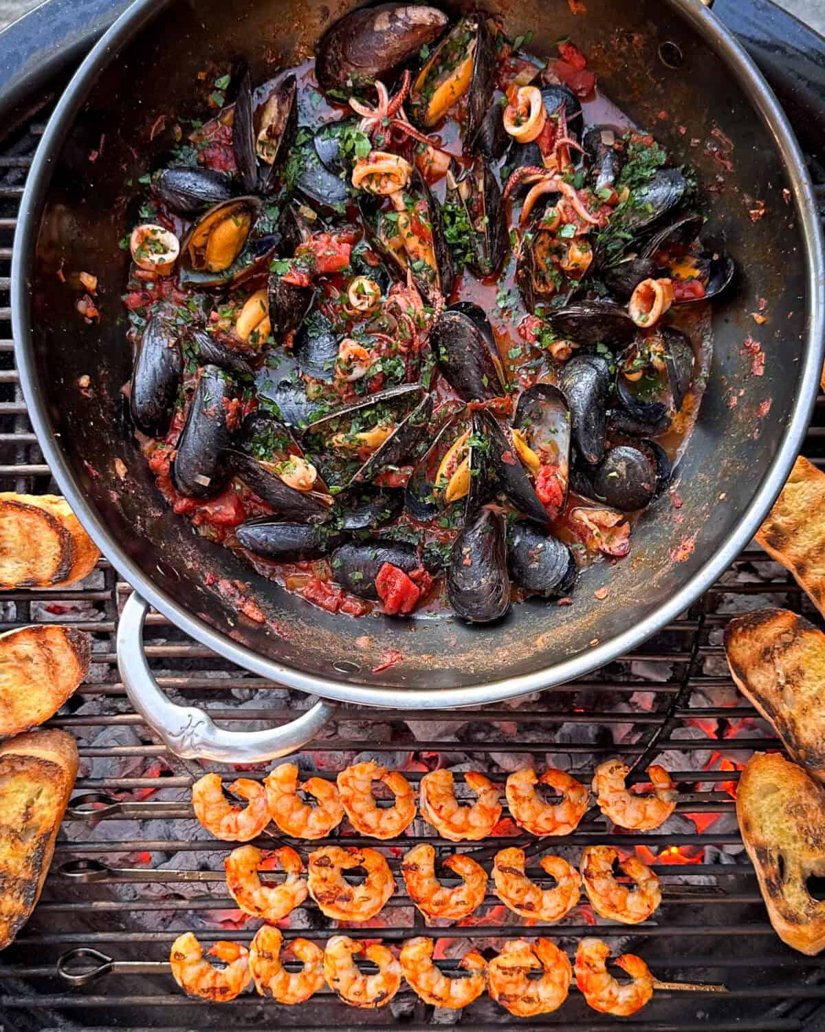 A large wok over the BBQ with Spicy 'Nduja Seafood in Tomato Broth, with shrimp skewers and baguette toasts.