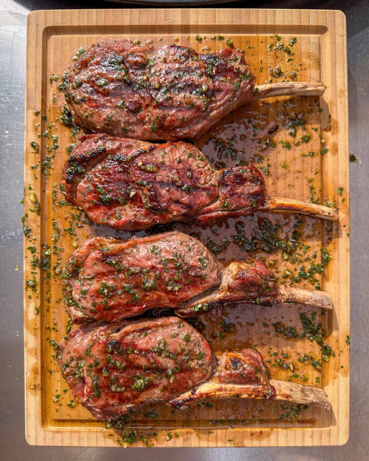 Four veal chops resting on a cutting board with board sauce.