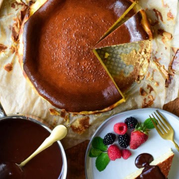 A burnt basque cheesecake with a slice removed. Served with a chocolate sauce, berries, mint and edible flowers.
