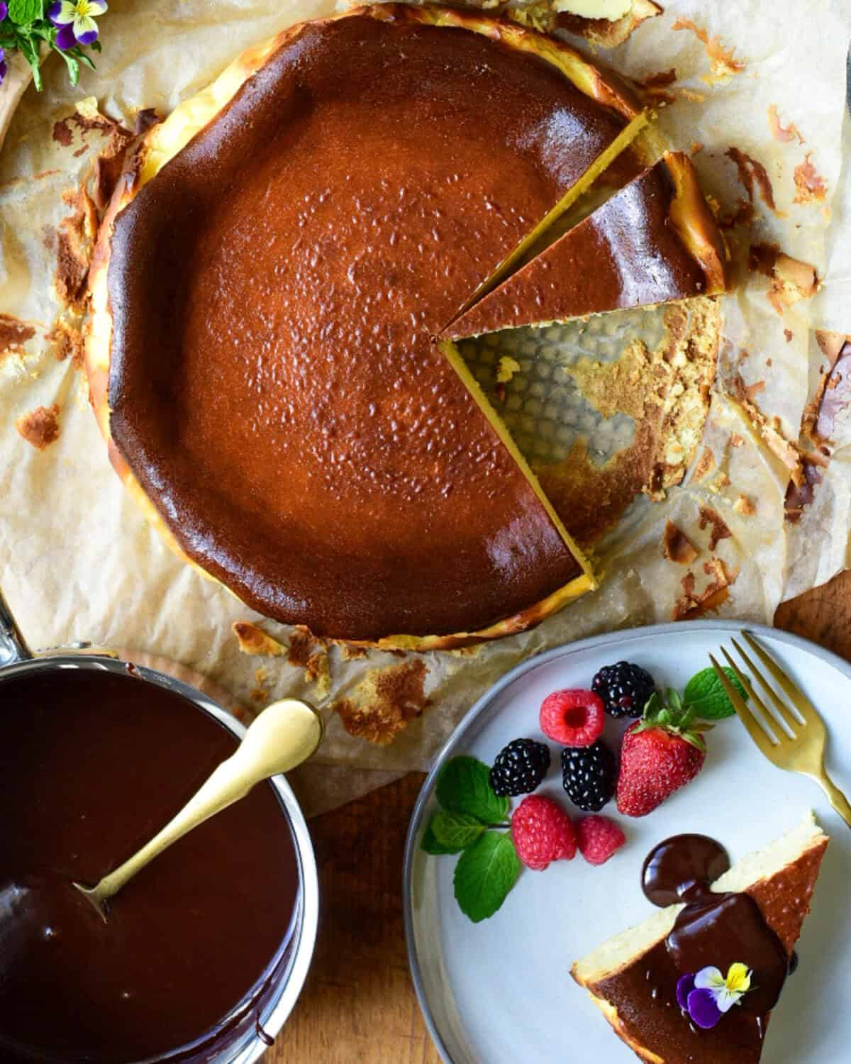 A burnt basque cheesecake with a slice removed. Served with a chocolate sauce, berries, mint and edible flowers.