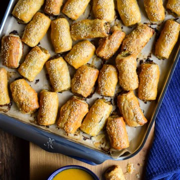 A tray of Pork, Fennel and Apple Sausage Rolls with a bowl of honey mustard dipping sauce.