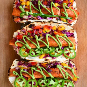 Three very colourful Air Fryer Salmon Tacos with Mango Slaw & Avocado Crema.