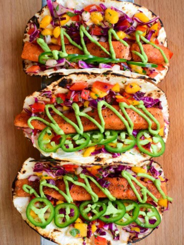 Three very colourful Air Fryer Salmon Tacos with Mango Slaw & Avocado Crema.