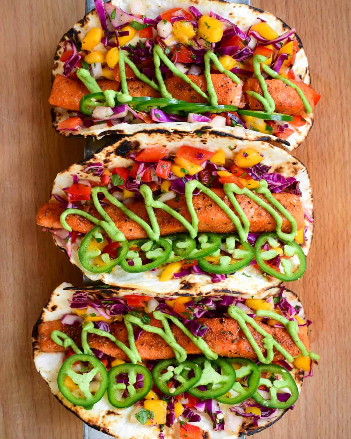 Three very colourful Air Fryer Salmon Tacos with Mango Slaw & Avocado Crema.