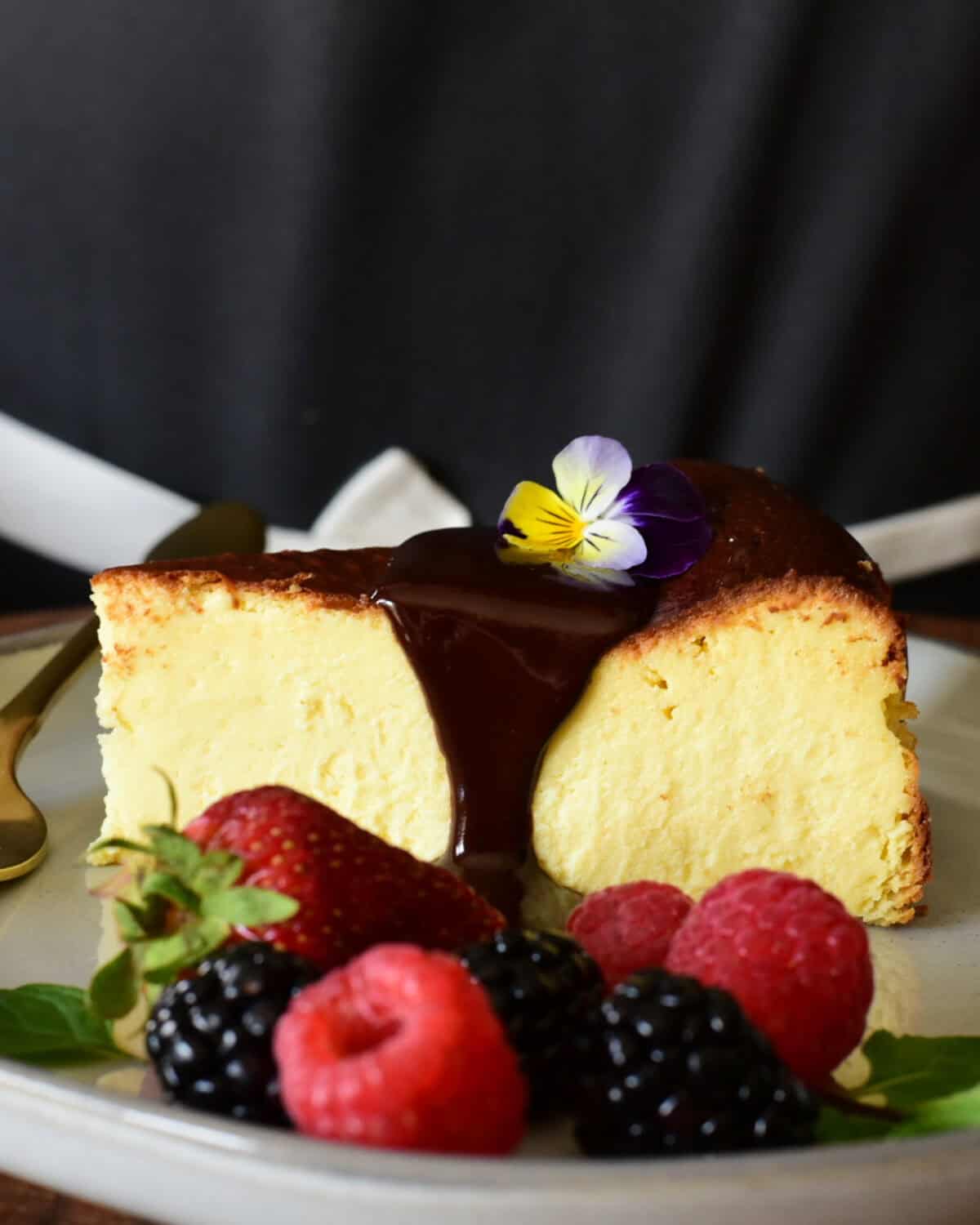 A slice of a basque baked cheesecake served with chocolate sauce, fresh fruit, mint and an edible flower.