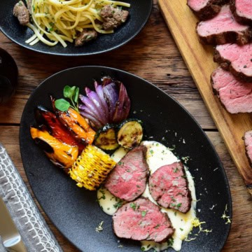 A dish with three peices of grilled veal butt tenderloin medallions on a lemon cream sauce served with grilled vegetables and a garlic butter veal tips linguine.