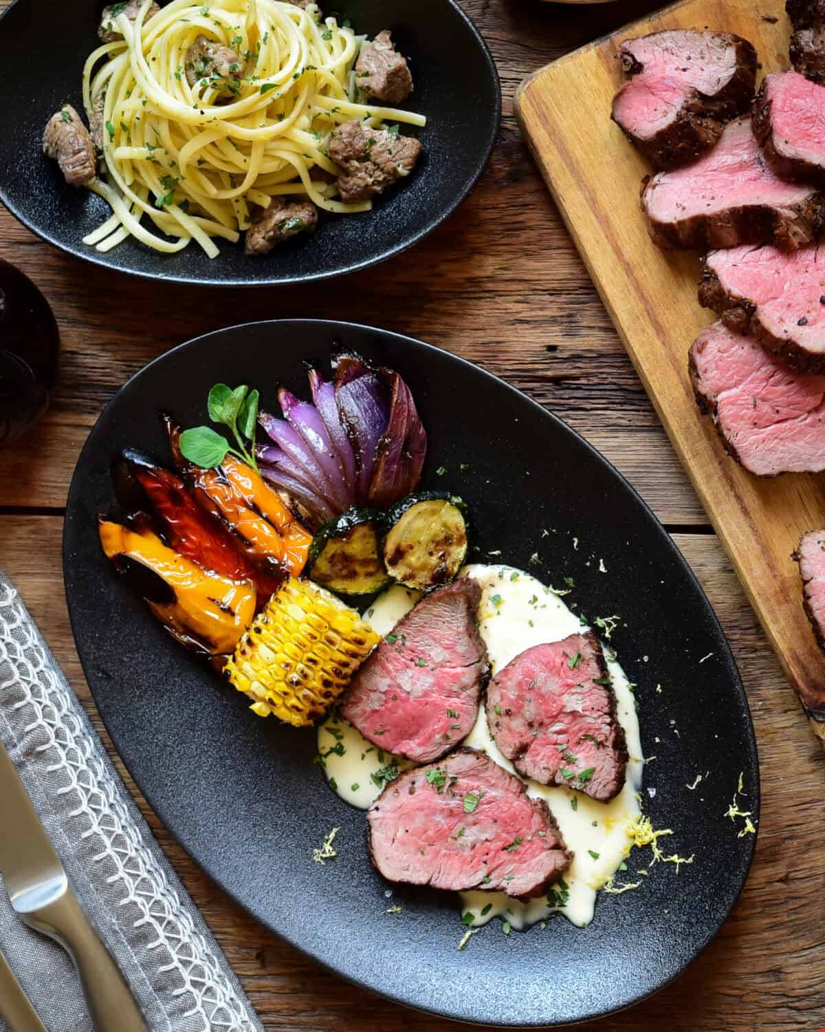 A dish with three peices of grilled veal butt tenderloin medallions on a lemon cream sauce served with grilled vegetables and a garlic butter veal tips linguine.