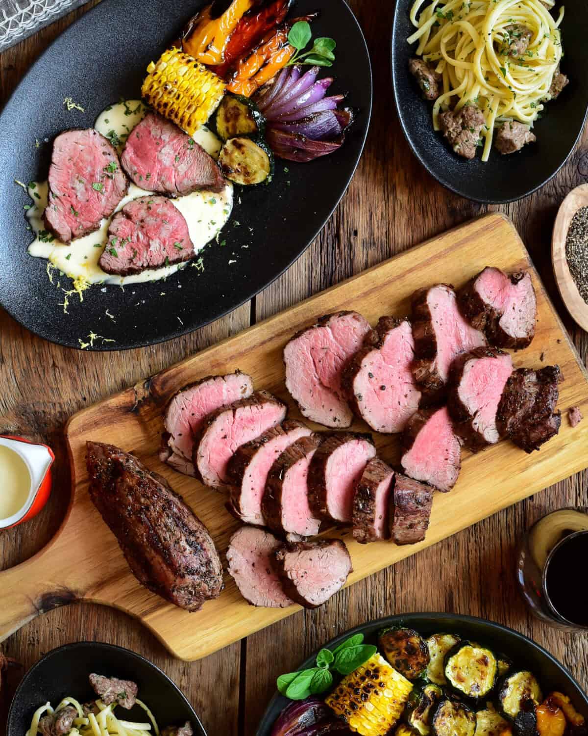 Slices of grilled veal tenderloin on a cutting board and a plated dish with veal medallions on a lemon cream sauce with grilled vegetables.