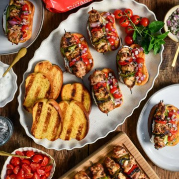 A platter of grilled chicken souvlaki on Texas Toast with extra grilled toast and more skewers on the side.