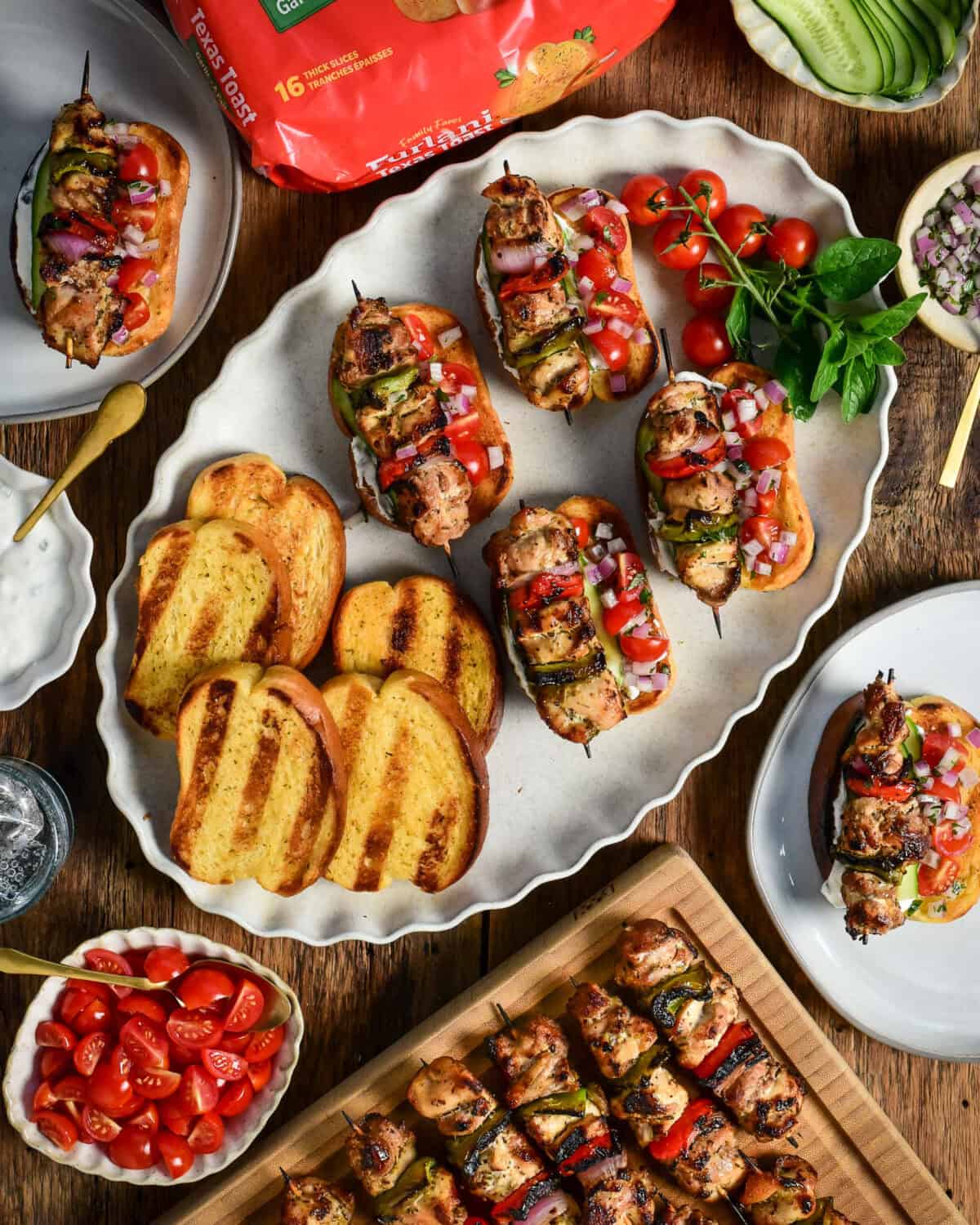 A platter of grilled chicken souvlaki on Texas Toast with extra grilled toast and more skewers on the side.