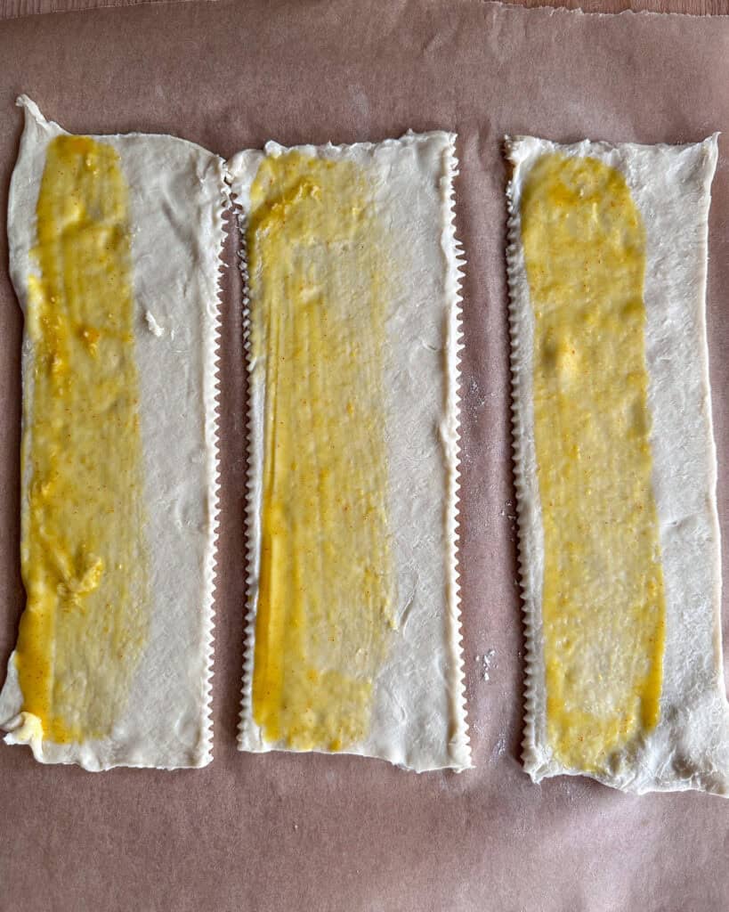 Three strips of puff pastry with a honey mustard sauce brushed on one side.