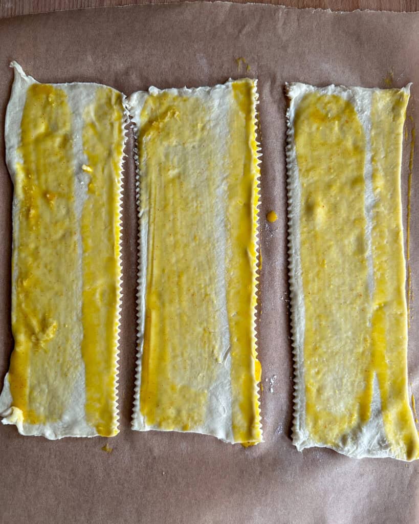 Three strips of puff pastry each with a stripe of honey mustard sauce and egg wash.