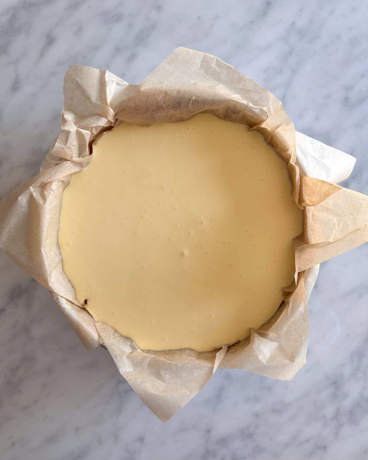 A parchment lined pan with batter for an easy burnt basque cheesecake recipe.