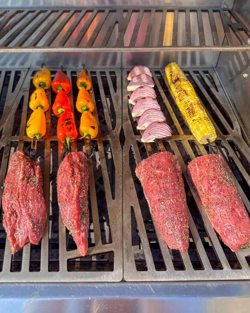 Veal on the grill with veggie skewers in the back.