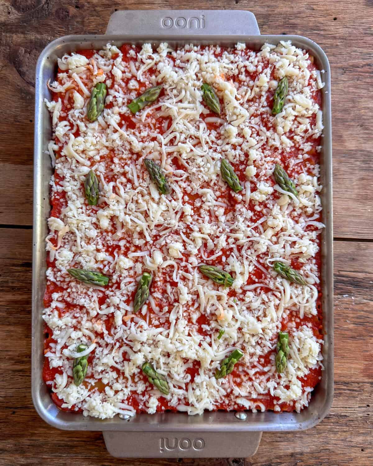 A lasagna tppped with cheese, tomato sauce and asparagus spears ready to bake.