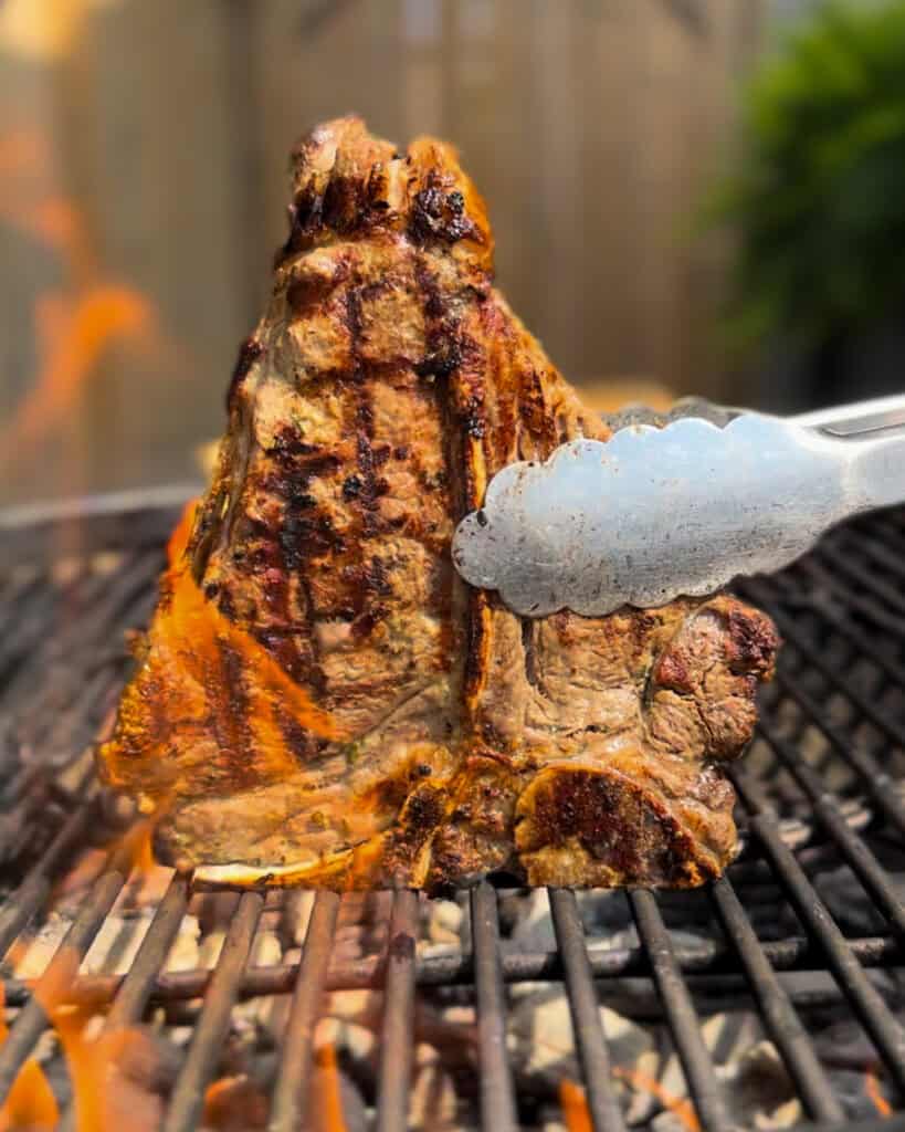 A grilled veal loin chop on the grill with flames and grill marks.