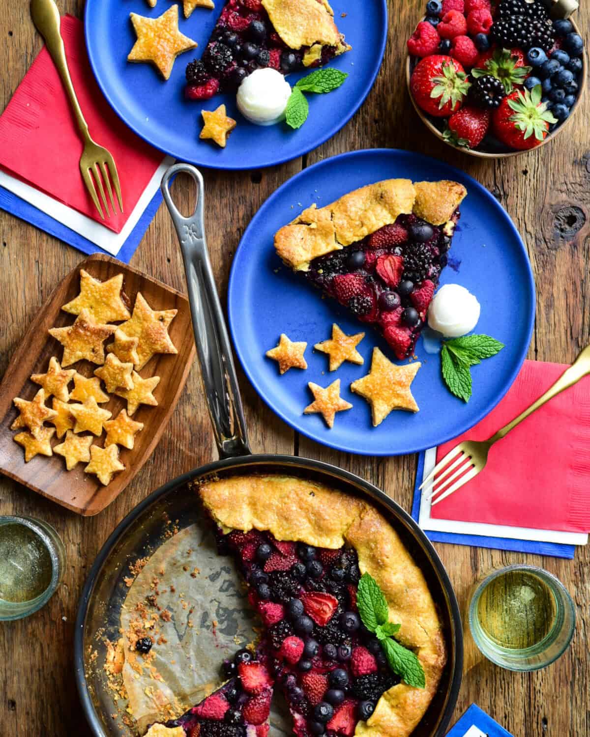 A grilled mixed berry gallet in a pan with two servings on blue plates with stars made from the crust and served with ice cream.