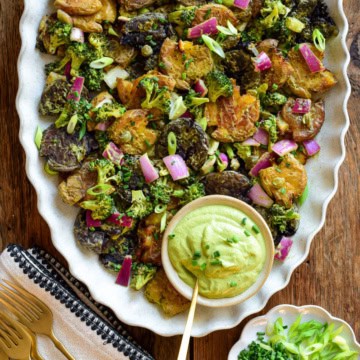 A platter of Crispy Smashed Potato Salad with a bowl of avocado dressing.