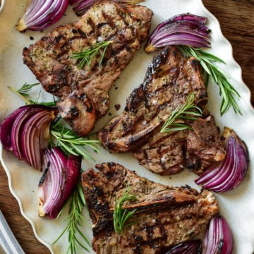 A platter with three grilled veal t-bone chops with grilled red onions and rosemary.