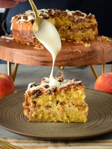 A slice of Air Fryer (Peach) Coffee Cake getting drizzled with icing with the cake in the background.