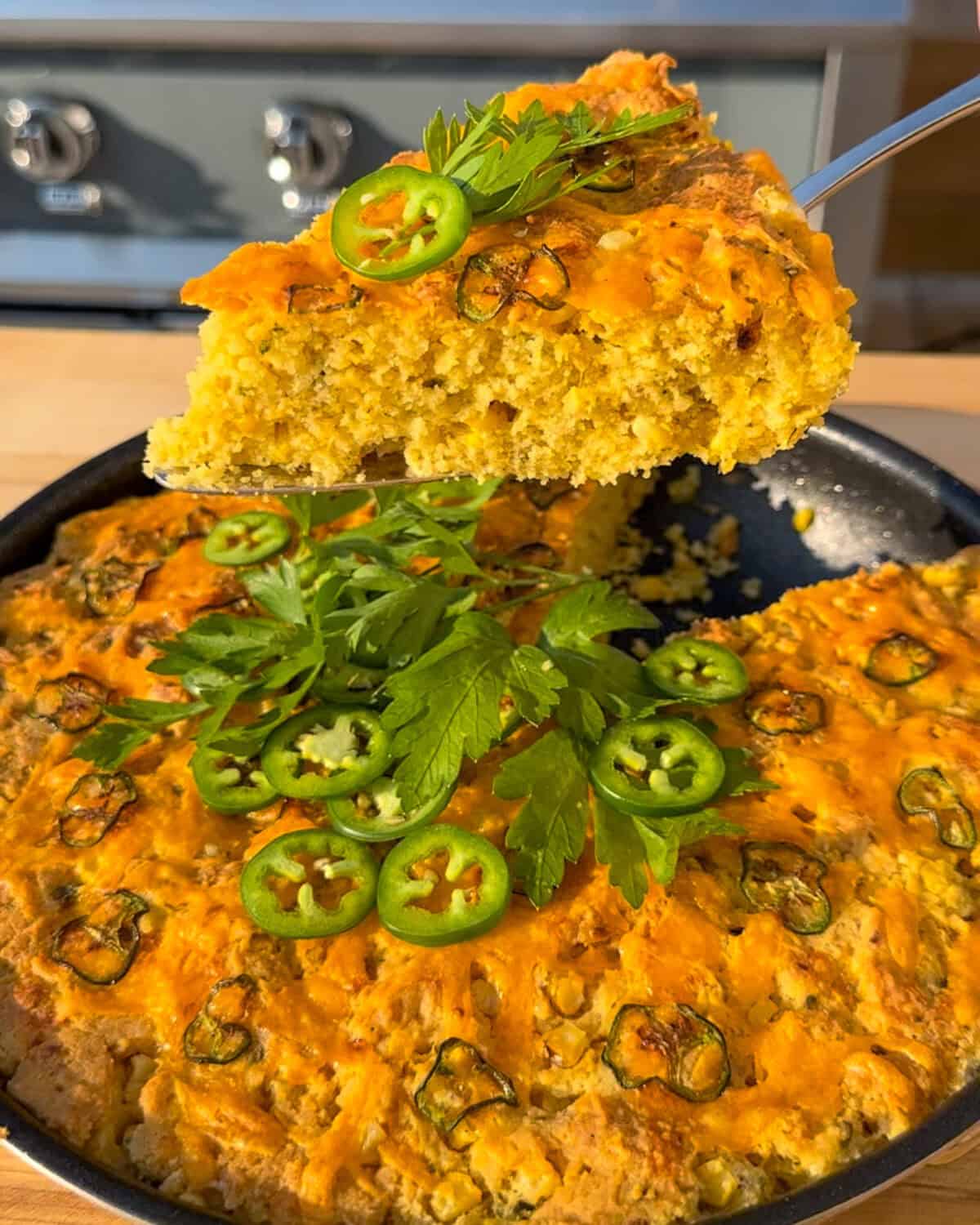 A slice of skillet jalapeno cheddar cornbread being lifted up. The cornbread is topped with fresh parsley and jalapenos.
