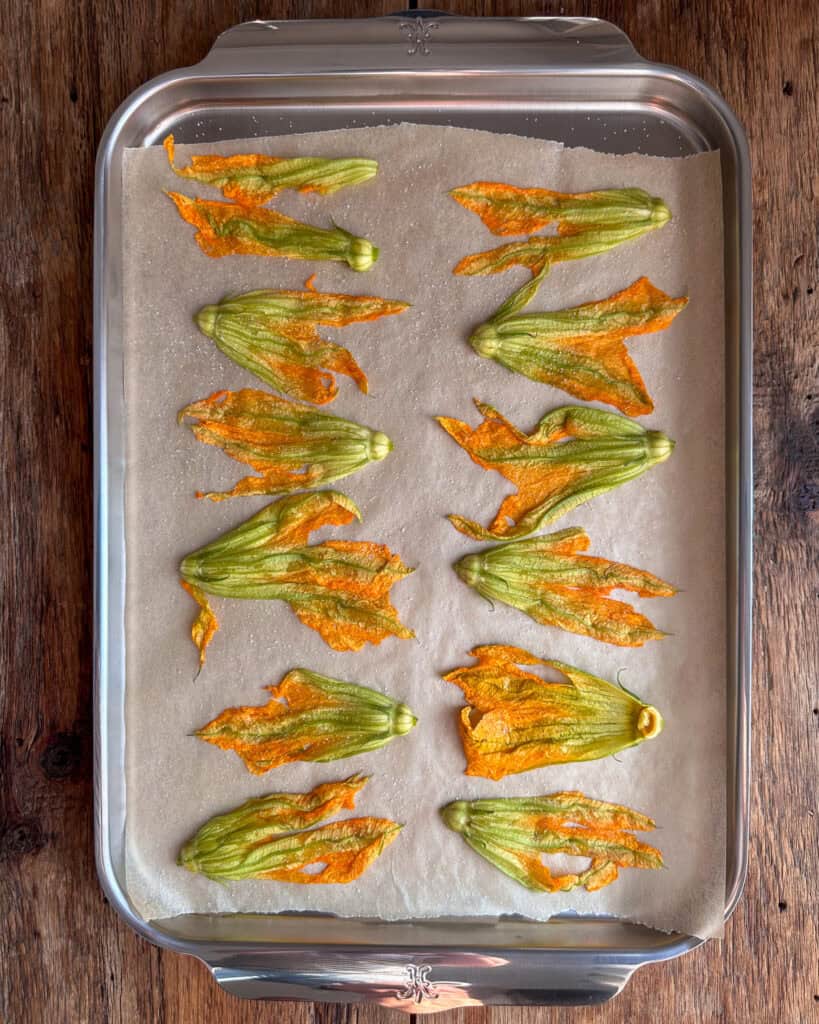 Zucchini blossoms lightly coated in oil and spinkled with sugar on a sheet pan.