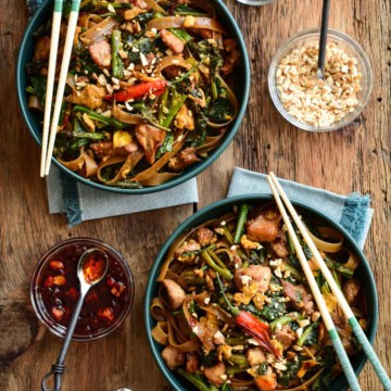 Two bowls of Thai Chicken Stir Fry with Rice Noodles with chopsticks and toppings on the side.