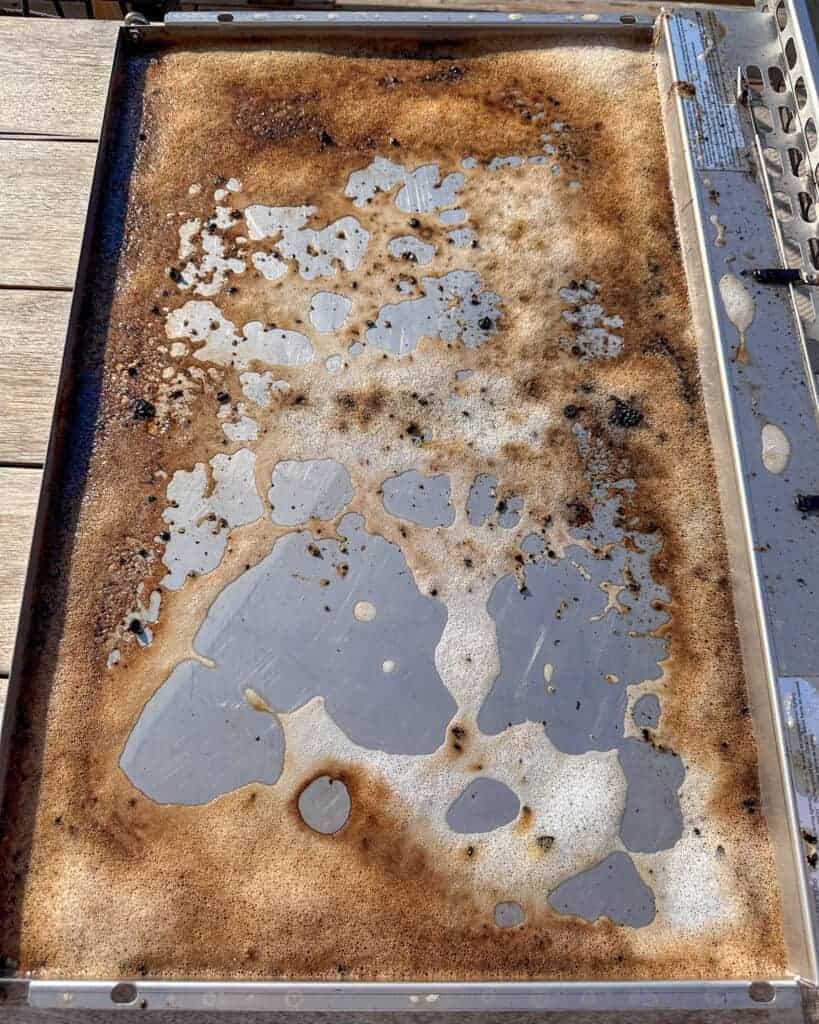 How to clean a gas grill drip pan - place the tray on a flat surface and spray with a grease cleaner.