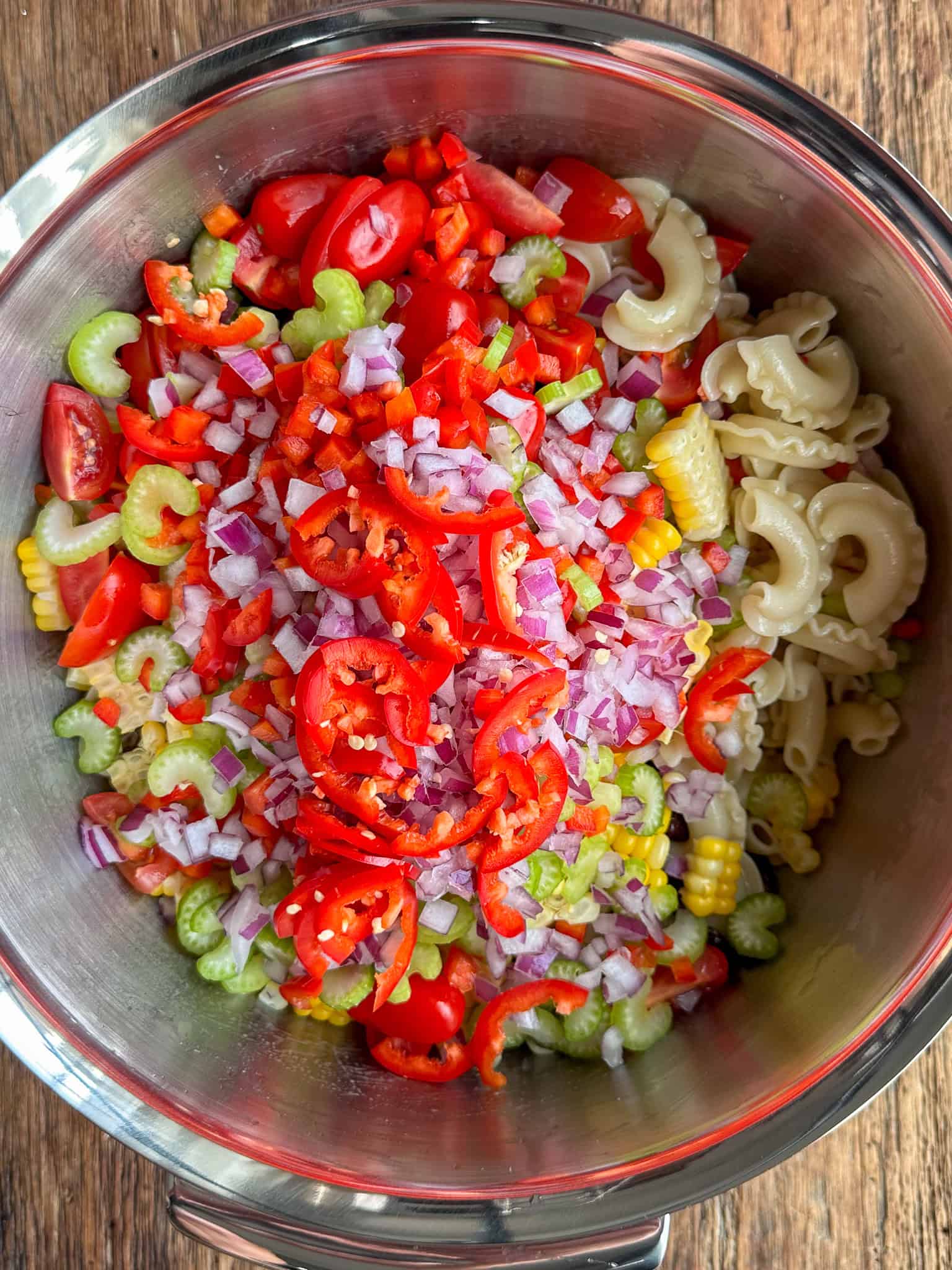 A bowl with the cooked macaroni, combine the grilled corn kernels, grape tomatoes, red pepper, celery, black beans, red onion and jalapeño.