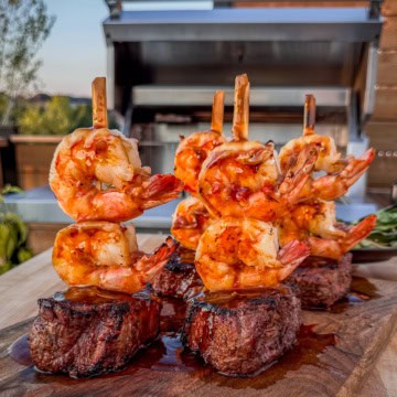 Four strip loin steaks each skewered with two shrimps and coated with teriyaki sauce.