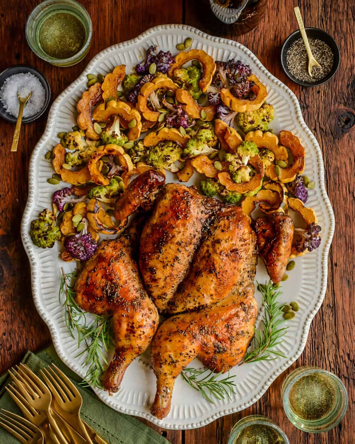 An herb butter spatchcock chicken on a platter with with roasted delicata squash and cauliflower.