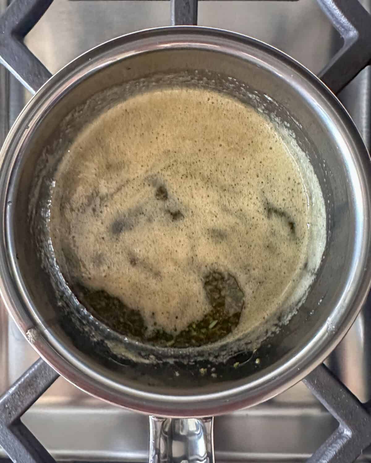 A small saucepan with melted butter, chopped rosemary and maple syrup.