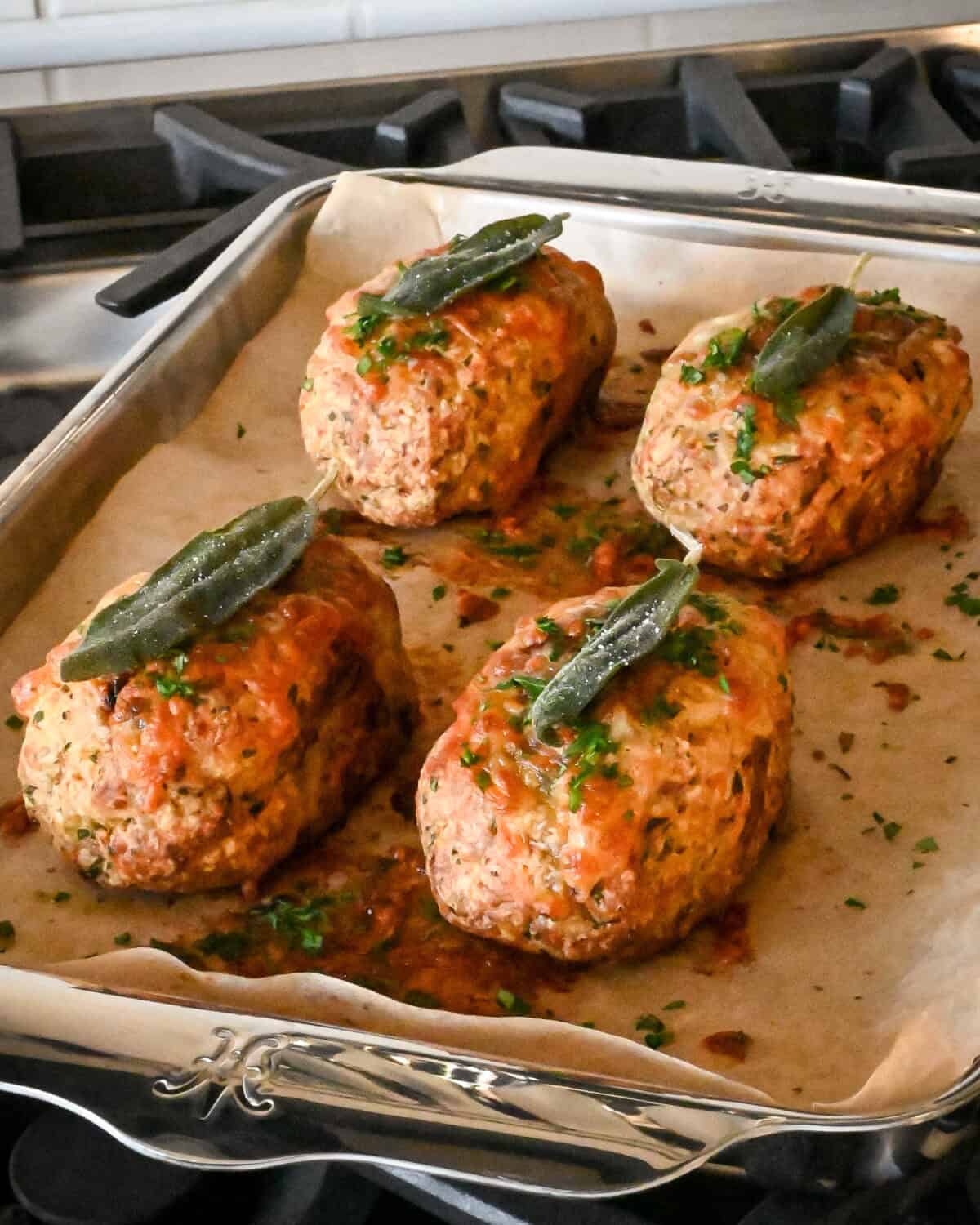 Four individual turkey meatloaves on a pan each with a fried sage leaf.