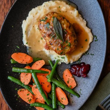 An individual turkey meatloaf served with mashed potatoes, gravy and vegetables.
