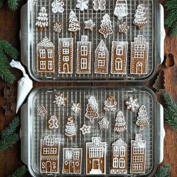 Two sheet pans with gingerbread cookies, piped with royal icing and sprinkled with icing sugar.