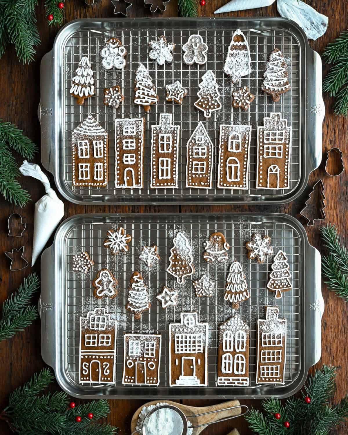 Two sheet pans with gingerbread cookies, piped with royal icing and sprinkled with icing sugar. 