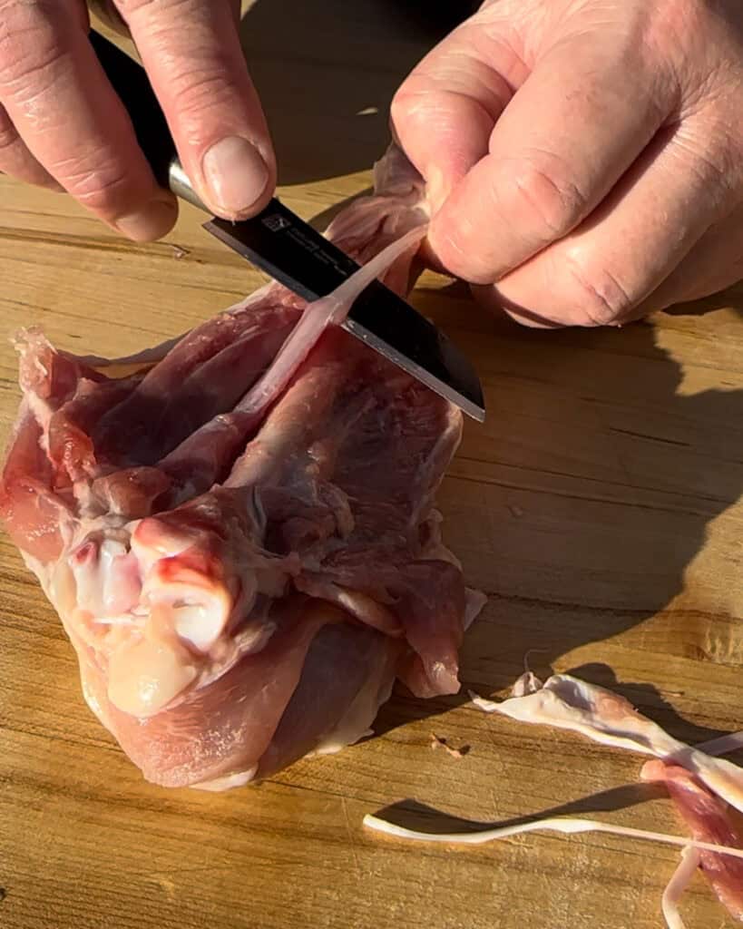 Locate the tough white tendons within the leg. Use kitchen shears or a knife to carefully snip as many as you can out.