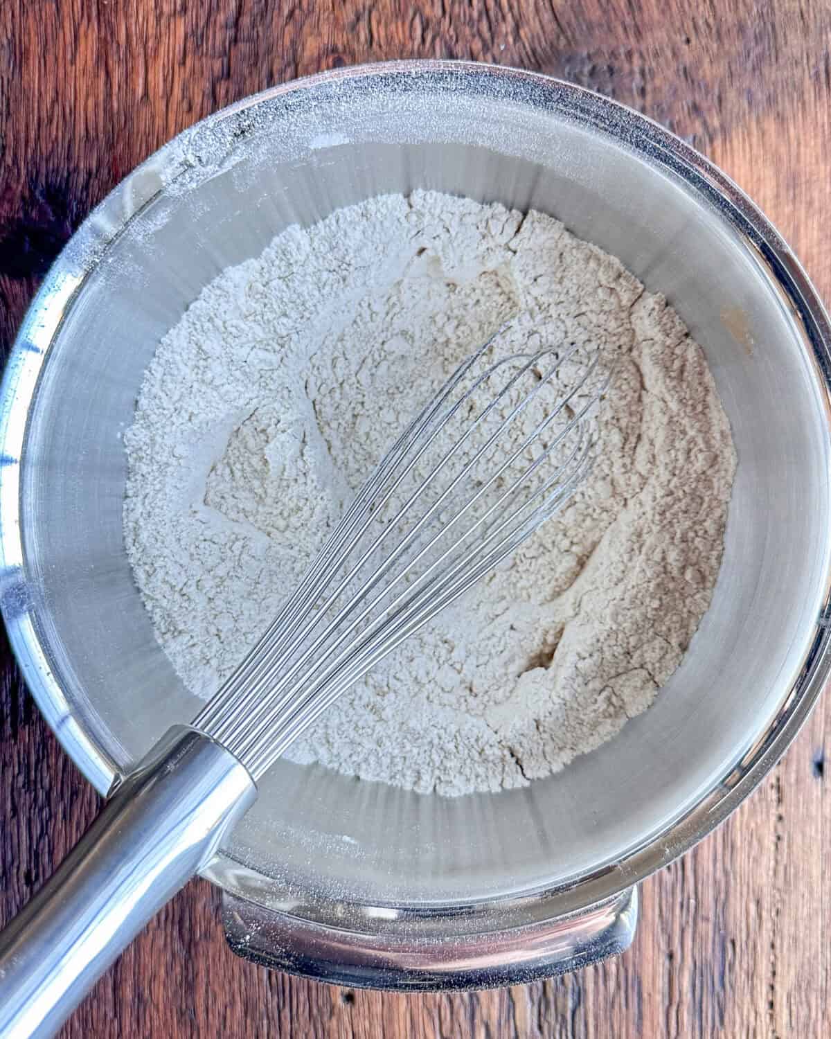 A bowl with flour, cinnamon, baking soda, ground ginger powder, salt and grated nutmeg mixed with a whisk.