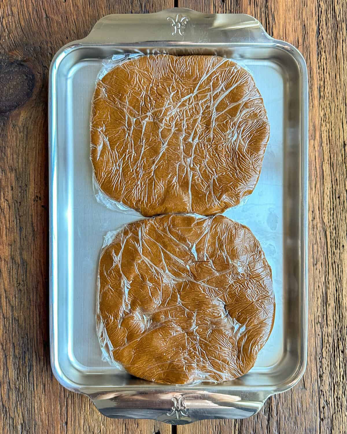 Two disks of gingerbread dough wrapped in plastic to be placed in the refrigerator.