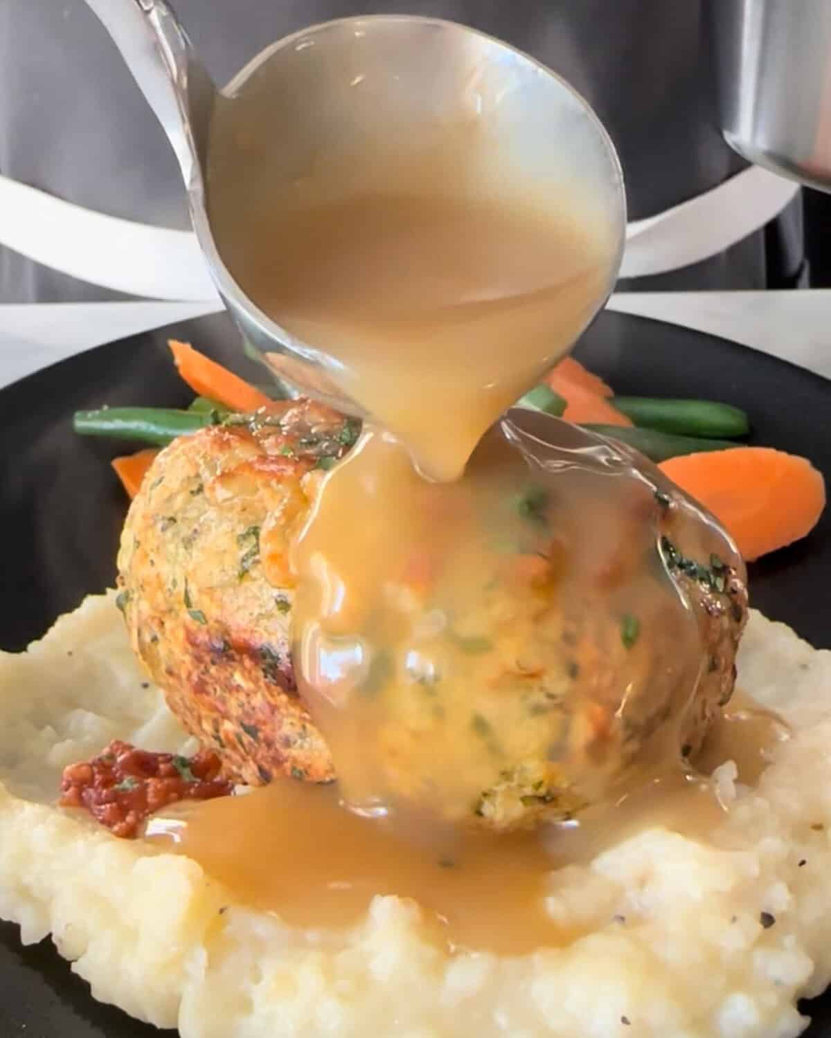 Gravy is being poured over an individual turkey meatloaf placed on mashed potatoes.