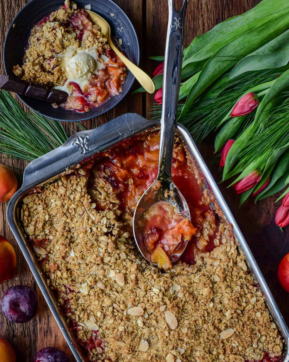 A stone fruit and cranberry fruit crisp in a baking dish with a portion served with ice cream.
