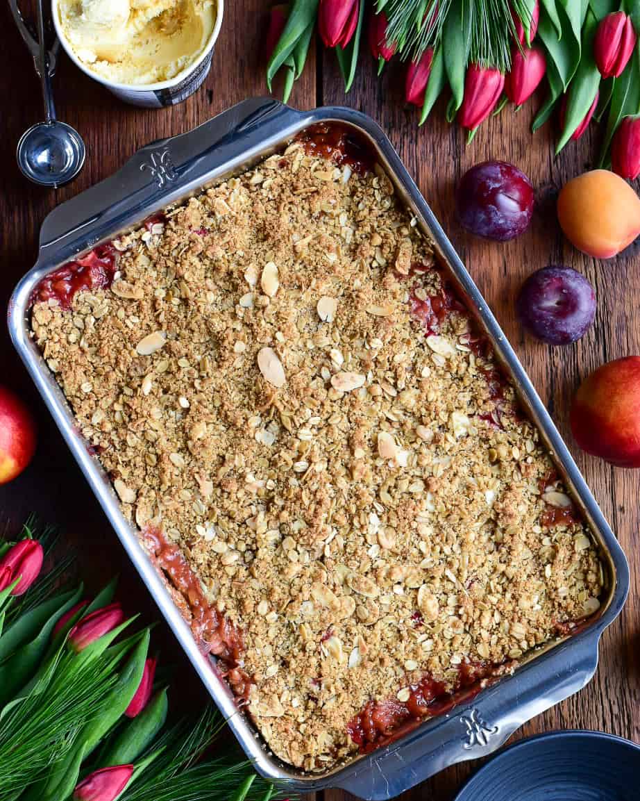 A stone fruit and cranberry fruit crisp in a baking dish with a portion served with ice cream.